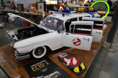 Highly detailed model of the Ghostbusters ECTO-1 with open hood and doors, surrounded by memorabilia including socks and a product manual.