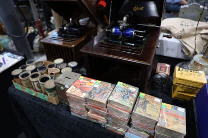 Two antique Edison-style cylinder phonographs on display alongside vintage cylinder record tubes and a stack of 1940s-50s Western pulp story reprints such as Buffalo Bill and Red Rider.