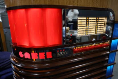 Close-up of a Gabel Kuro jukebox showing glowing red pilasters, chrome selector panel, and amber-lit title strip windows.