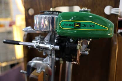 Restored vintage outboard motor painted in John Deere green with yellow branding, displayed on a wooden stand.