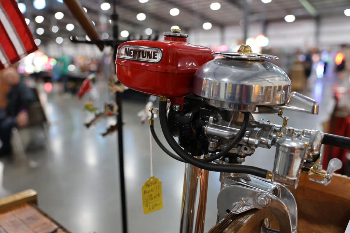 Close-up of a restored red Neptune outboard boat motor with chrome detailing and fuel lines, displayed indoors.