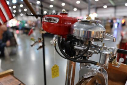Close-up of a restored red Neptune outboard boat motor with chrome detailing and fuel lines, displayed indoors.