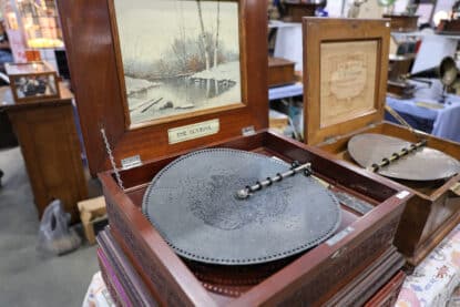 Antique Olympia disc music box with an ornate wooden case and metal perforated music disc, on display at the Chicagoland Coin-Op Show.