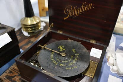 Antique Polyphon disc music box with German inscription and six-bell mechanism inside a polished wood case.