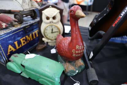 Vintage Red Goose Shoes advertising statue with an owl clock and antique toy car at a collector's show booth.