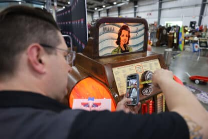 Person measuring and photographing a Rock-Ola Mystic Music jukebox at a collector event, capturing its vintage design and details.