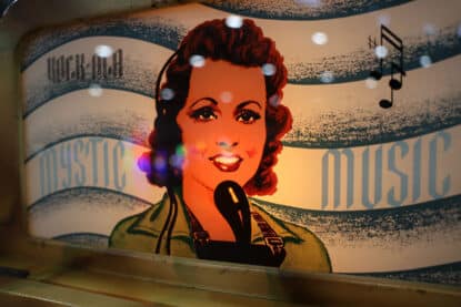 Close-up of Rock-Ola Mystic Music jukebox header glass featuring illustrated singer and musical notes.