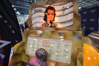 Close-up of the illuminated faceplate on the Rock-Ola Mystic Music jukebox featuring a 1940s-style female singer illustration and song selection card.