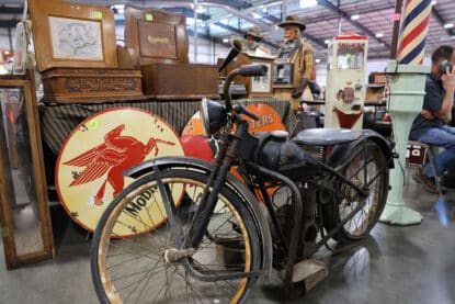 Vintage Simplex Automatic motorbike on display with Mobil Pegasus and Root Beer signs, antique phonographs, and coin-operated machines at the Chicagoland Coin-Op Show.