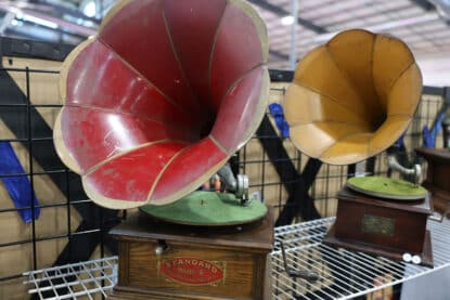 Pair of antique phonographs with colorful external horns - red and yellow - displayed on wire shelving. The front phonograph is labeled Standard Model A.