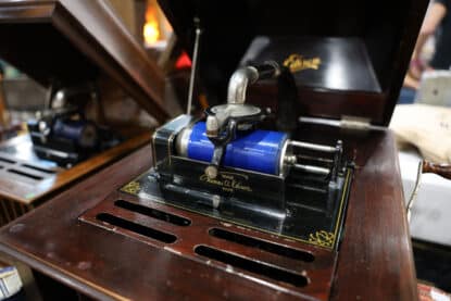 Close-up of an antique Thomas A. Edison cylinder phonograph with a bright blue wax cylinder record in a polished wooden case.