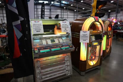 Three restored jukeboxes on display: a 1955 Seeburg VL200, a Rock-Ola CD Bubbler, and a Wurlitzer 1015, all lit and labeled for sale.