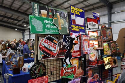 Mixed display of vintage advertising signs including Point Bock Beer, Red Man Racing, Raleigh cigarettes, and Marlboro, shown at the Chicagoland Coin-Op Show.