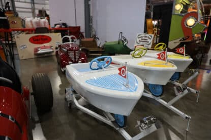 Restored vintage kiddie boat ride cars with steering wheels and flags on display.