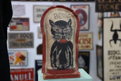 Hand-painted vintage carnival knockdown target labeled "Bessie" with a stylized black cat design and red leather trim.