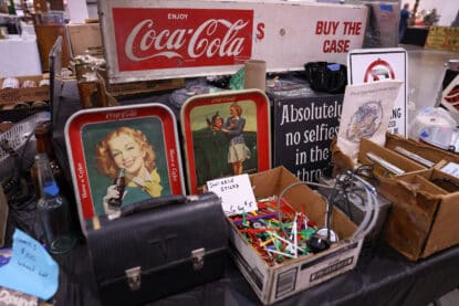 Vintage Coca-Cola trays, retro signs, and swizzle sticks on a collectibles table at an antique show.