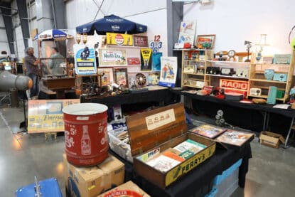 Booth display with vintage radios, soda advertising signs, ephemera, and retro memorabilia at an antique show.