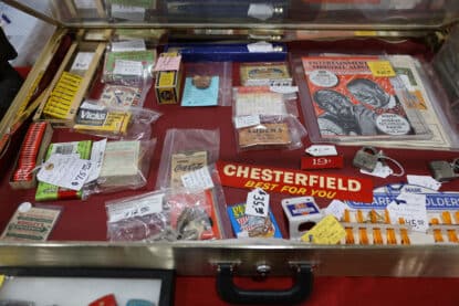 Display case of vintage items including Luden’s and Vicks cough drops, Chesterfield cigarette ads, Coca-Cola labels, locks, and advertising cards from the 1940s to 1960s.
