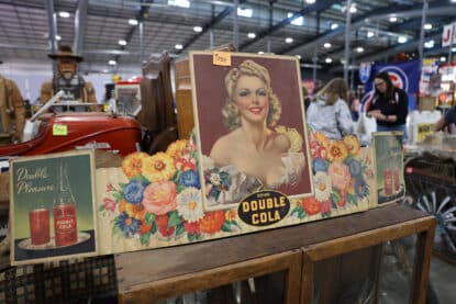 Colorful vintage Double Cola pin-up advertising sign with floral design and 1940s-style illustration, displayed at the Chicagoland Coin-Op Show.