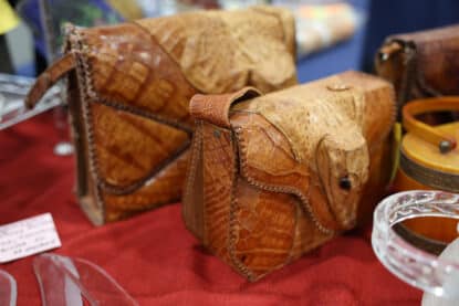Two vintage handcrafted purses made from exotic alligator or crocodile leather, displayed on a red fabric at an antique show.