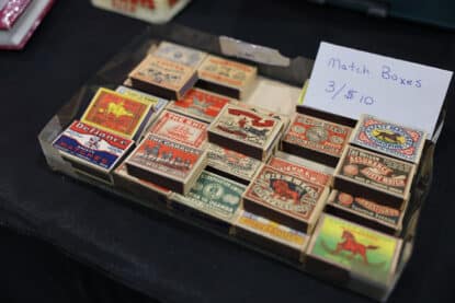 Collection of vintage matchboxes featuring bold graphic art and branding from Sweden and the USA, displayed in a tray with a handwritten price tag of 3 for $10.