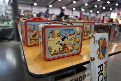 Vintage Looney Tunes lunchbox styled like a TV, featuring Sylvester, Tweety, and other classic cartoon characters, with additional Flintstones lunchboxes in the background.