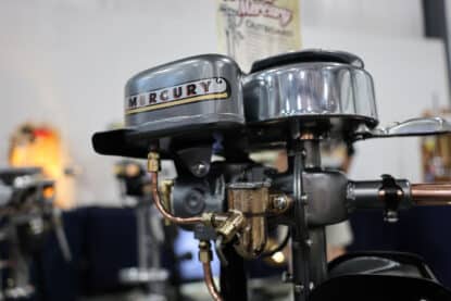 Close-up of a restored vintage Mercury outboard motor with metallic and chrome detailing, showcasing mechanical and fuel system components.