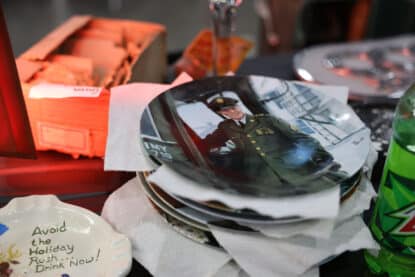 Stack of collectible Elvis plates next to a humorous holiday ashtray reading “Avoid the Holiday Rush - Drink Now!”