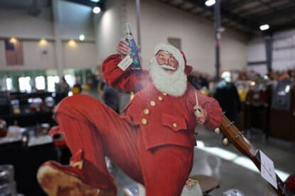 Vintage cardboard standee of Santa Claus holding a bottle of Pepsi with a holiday gift tag, on display at the Chicagoland Coin-Op Show.