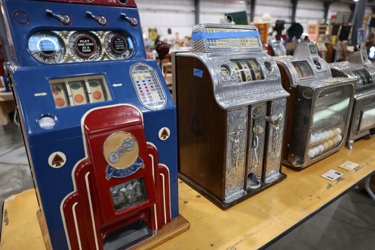 Lineup of vintage slot machines including colorful three-reel and ornate cast-iron models, on display at the Chicagoland Coin-Op Show.