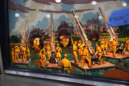 Illuminated vintage arcade game backglass depicting soldiers operating anti-aircraft guns with explosive battlefield action.
