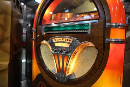 Close-up of a Wurlitzer 1015 jukebox with glowing pilasters and gold speaker grill.